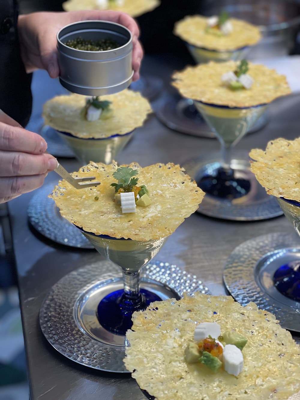 A chef garnishes delicate cheese and herb-topped cups of mousse with a sprinkle of caviar.