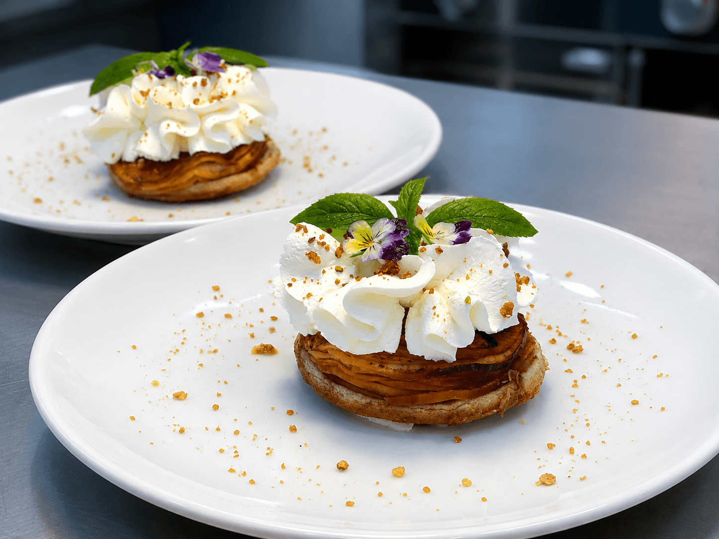 Two elegantly plated pastries topped with whipped cream, mint leaves, and edible flowers.