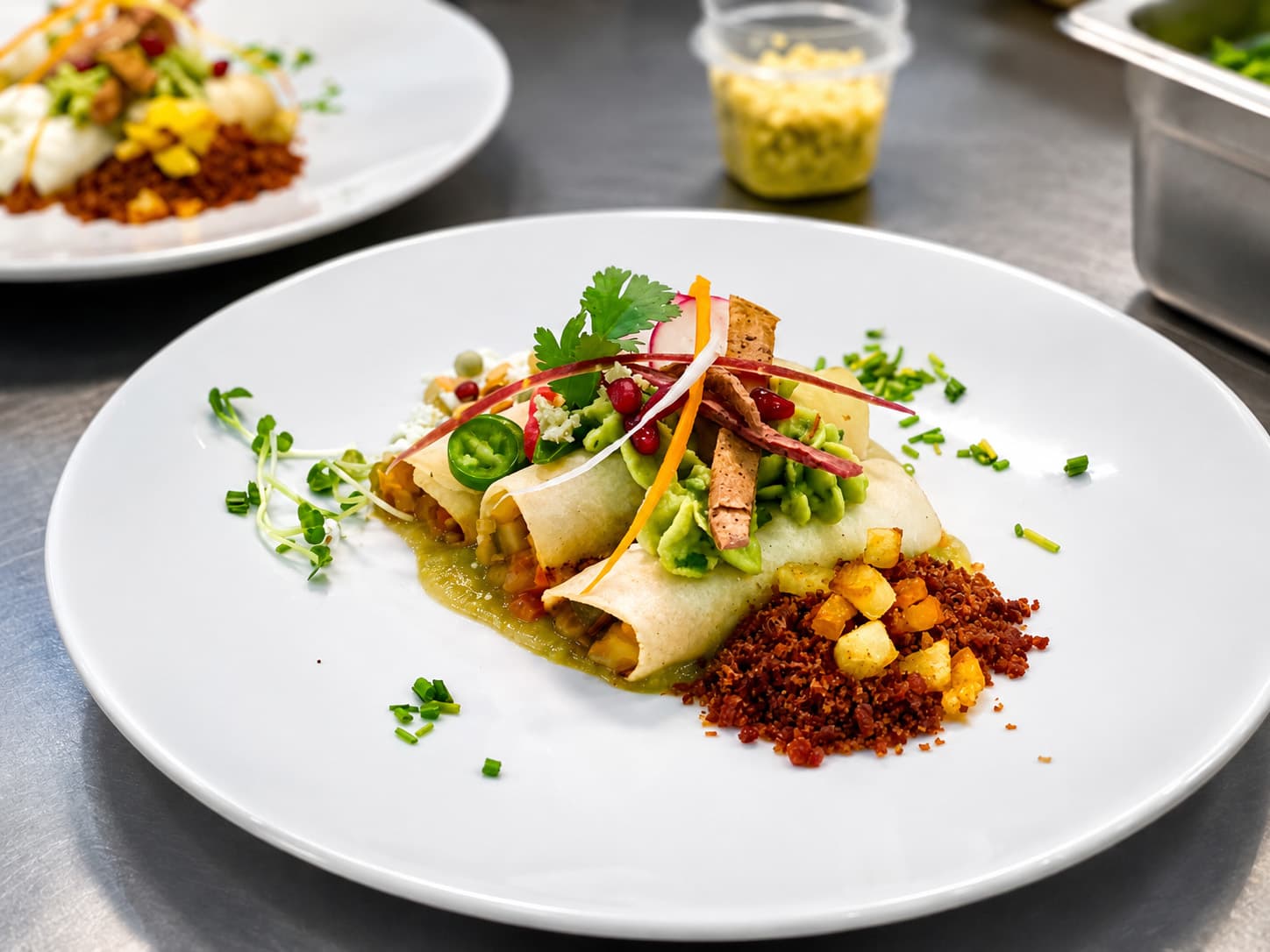 A plate of enchiladas topped with guacamole, vegetables, and garnishes, served with a side of spiced potatoes.