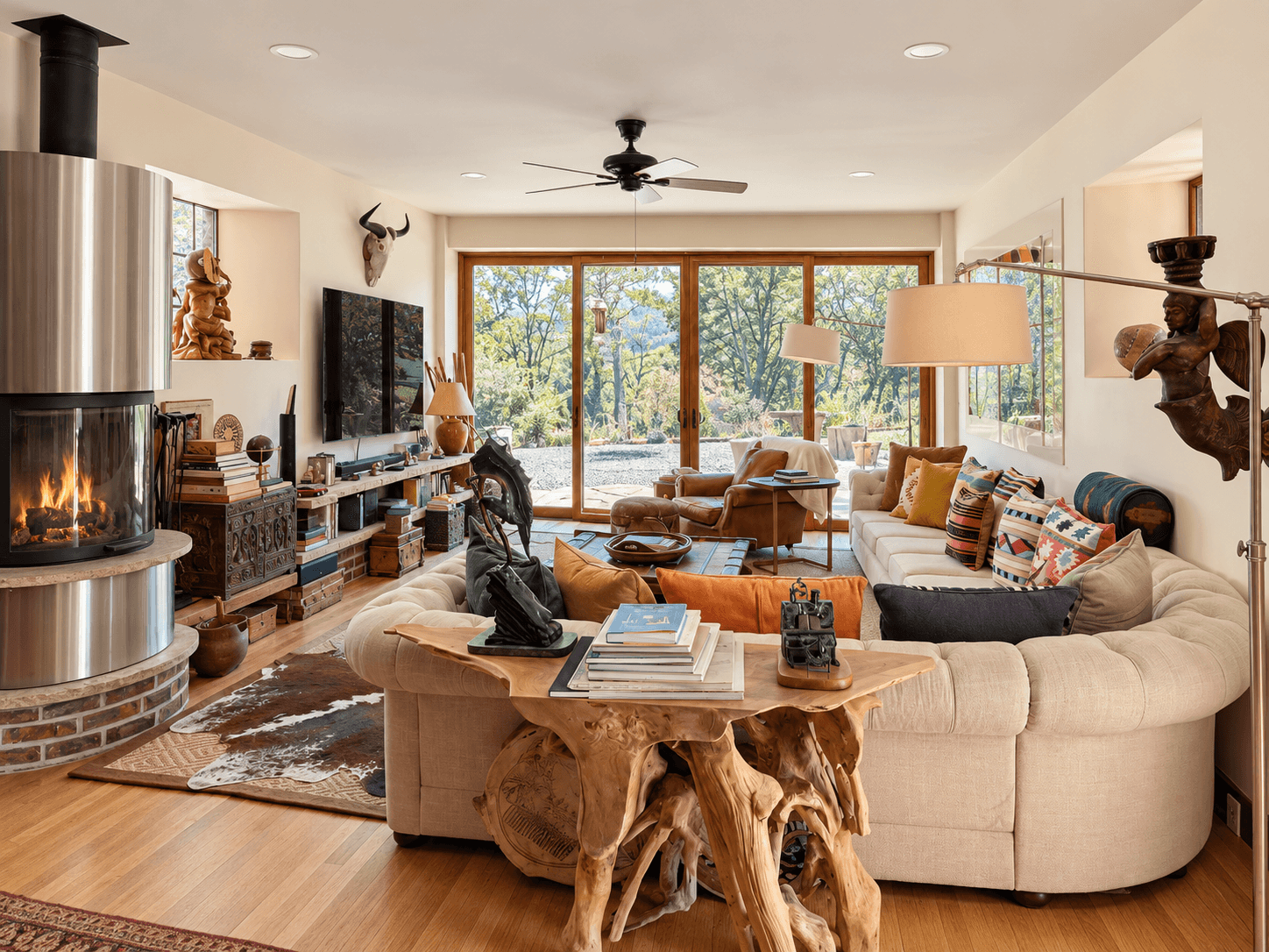 A cozy, modern living room features a stone fireplace, comfortable seating, and large windows overlooking a natural landscape.