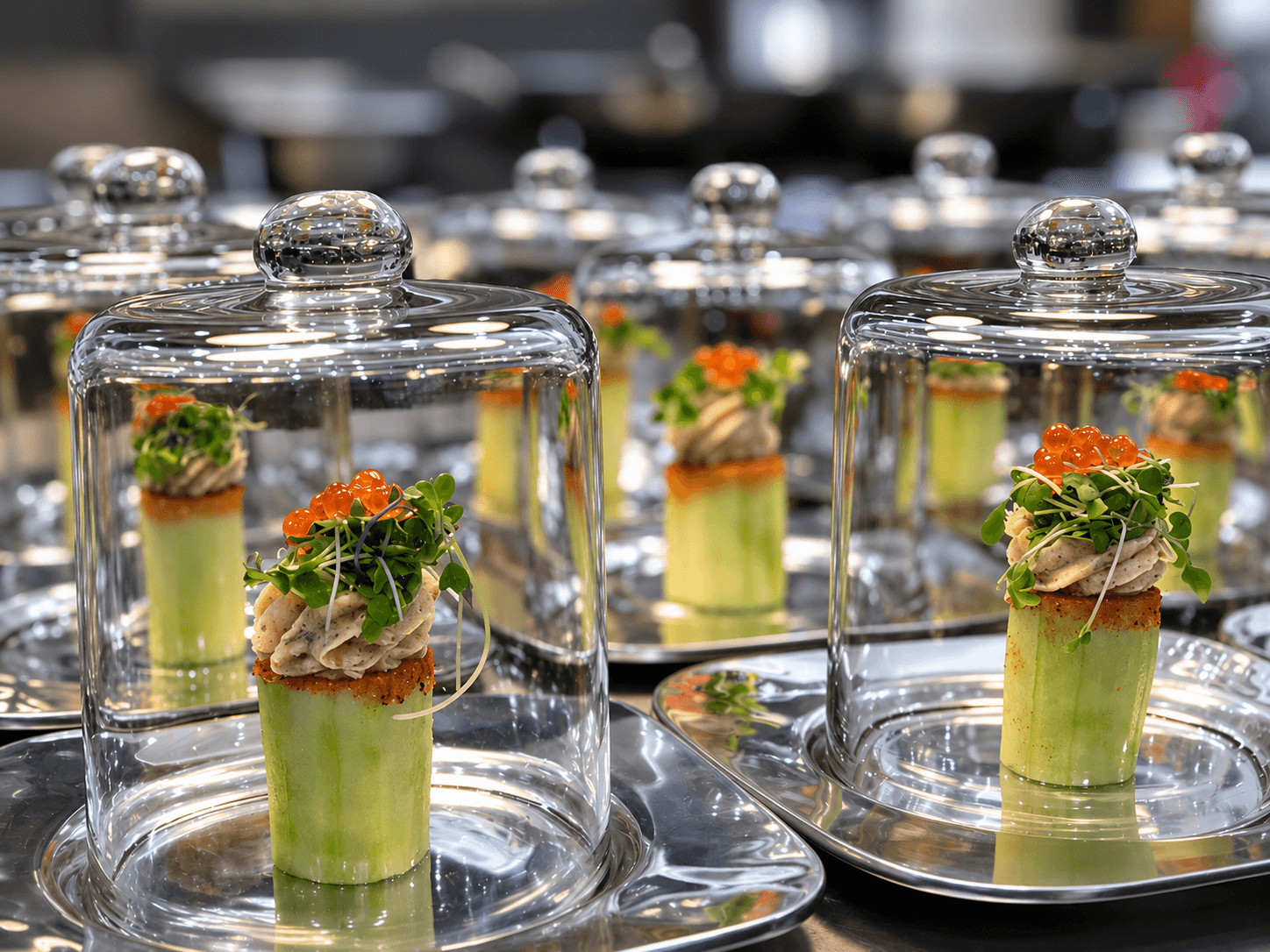 Elegant appetizer servings under glass cloches on silver plates.