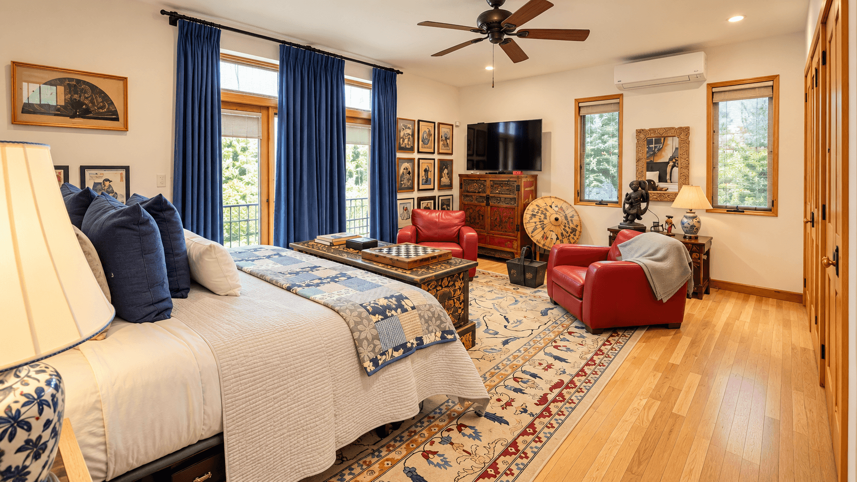 A cozy bedroom featuring a large bed, red armchairs, a flat-screen TV, and decorative art on the walls.