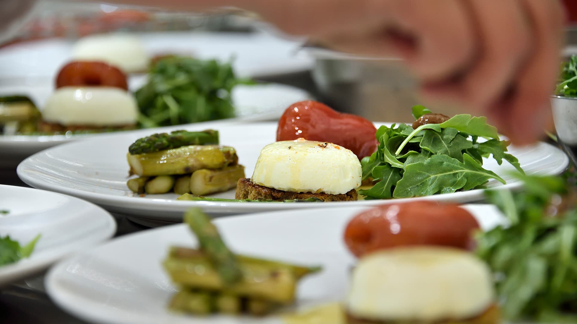 Plates of gourmet food featuring a soft cheese, tomatoes, asparagus, and arugula.