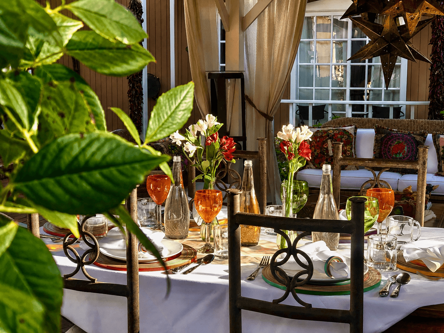 A beautifully set outdoor dining table adorned with colorful flowers and elegant glassware, framed by lush greenery.