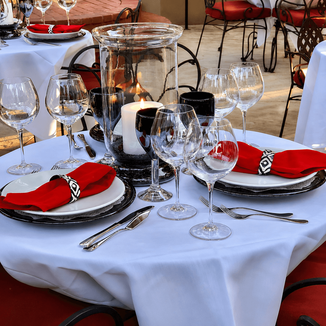 A elegantly set table with white tablecloth, red napkins, wine glasses, and a candle centerpiece.
