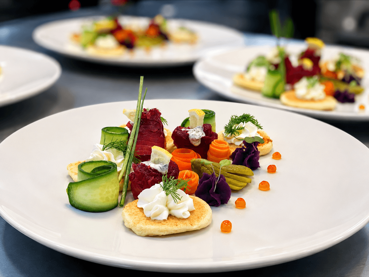 A beautifully arranged plate of colorful vegetables and cream on small pancakes, garnished with herbs and drizzled with sauce.