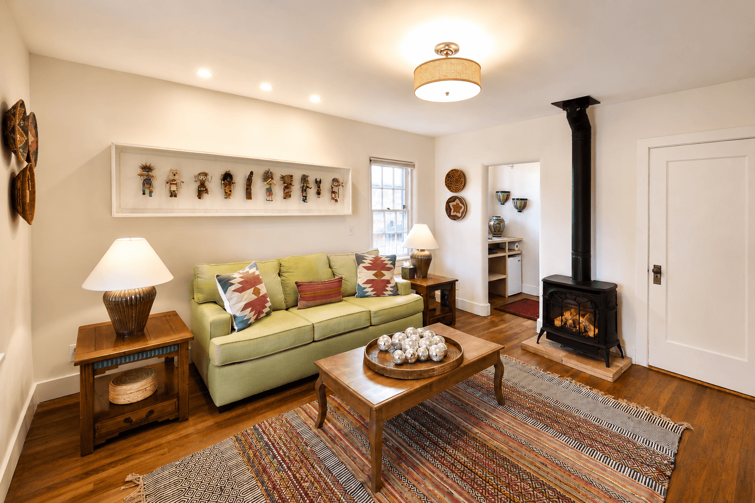 Cozy living room featuring a green sofa, wooden furniture, a small stove, and decorative wall art.