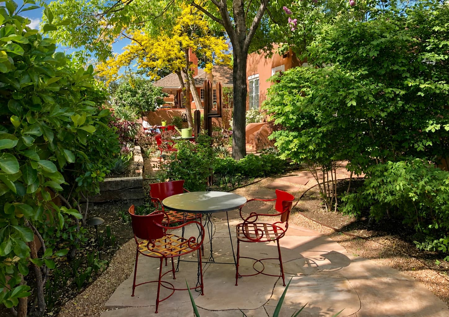 A quaint outdoor patio with red chairs and a round table surrounded by lush greenery.