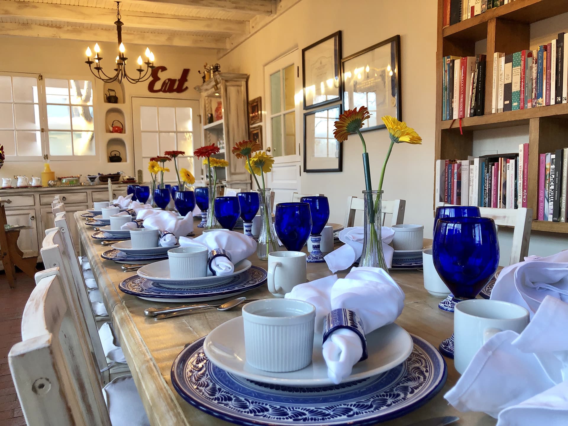 A beautifully set dining table with blue glassware, white dishes, and colorful flowers in a warm, inviting room.