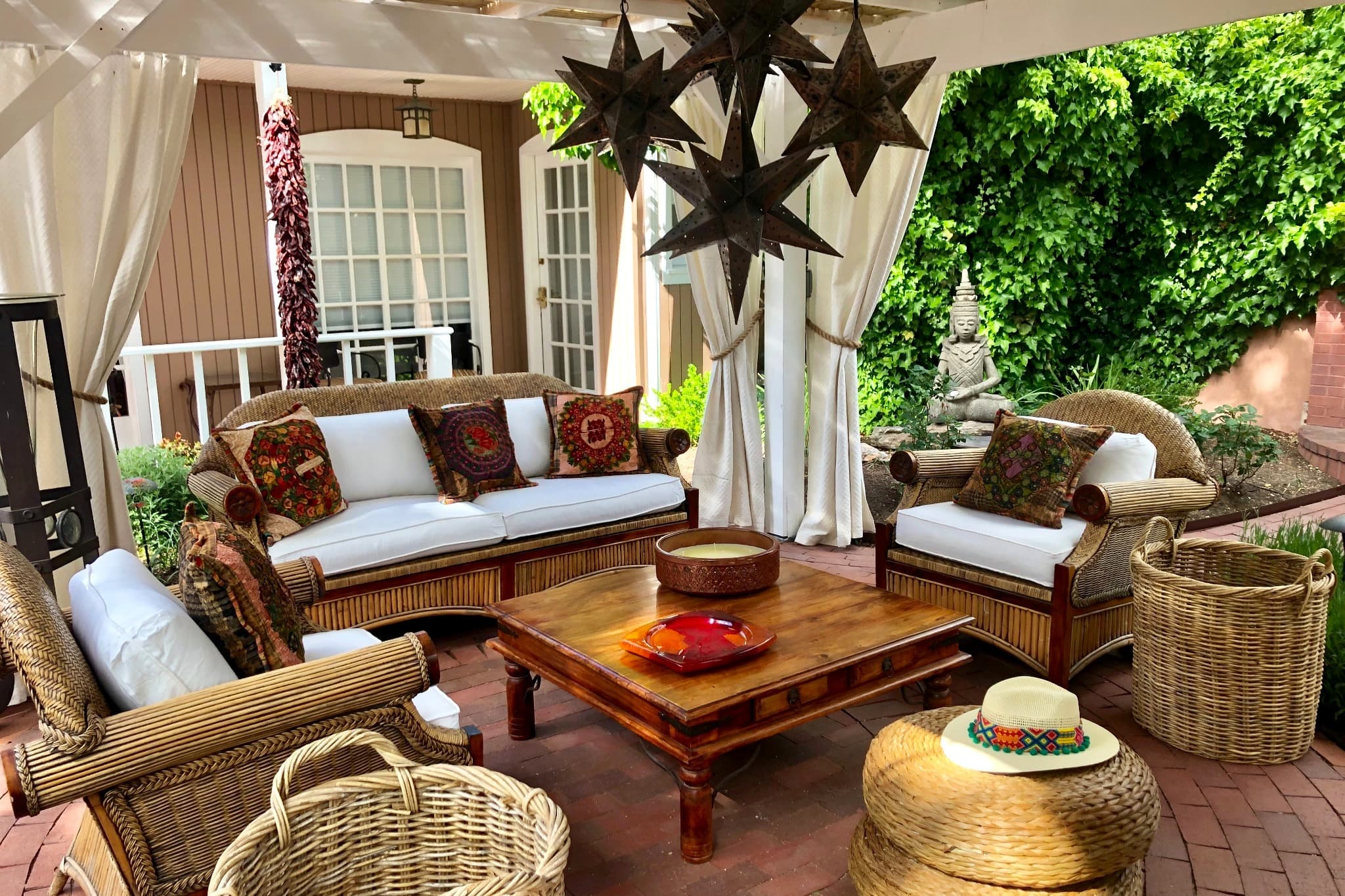 A cozy outdoor sitting area with wicker furniture, colorful cushions, and a wooden coffee table under a pergola.
