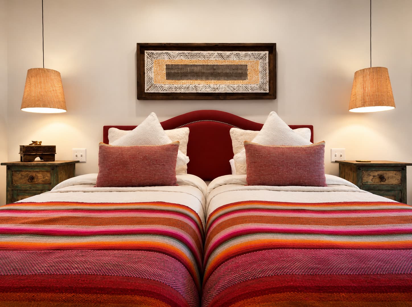 A cozy bedroom featuring two twin beds with colorful striped blankets and pendant lights.