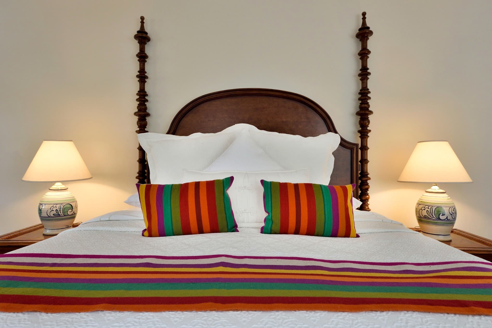 A cozy bed with colorful striped pillows and matching blanket, flanked by lamps.