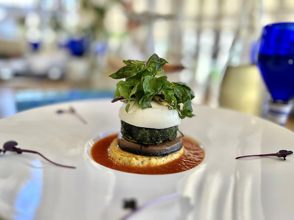 A gourmet dish featuring layered vegetables topped with fresh greens and served on a vibrant sauce.