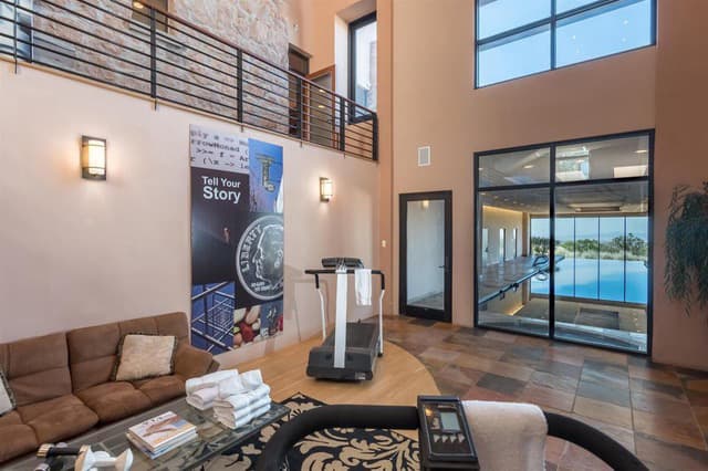A modern, stylish interior featuring a treadmill, cozy seating area, and large windows overlooking a pool.
