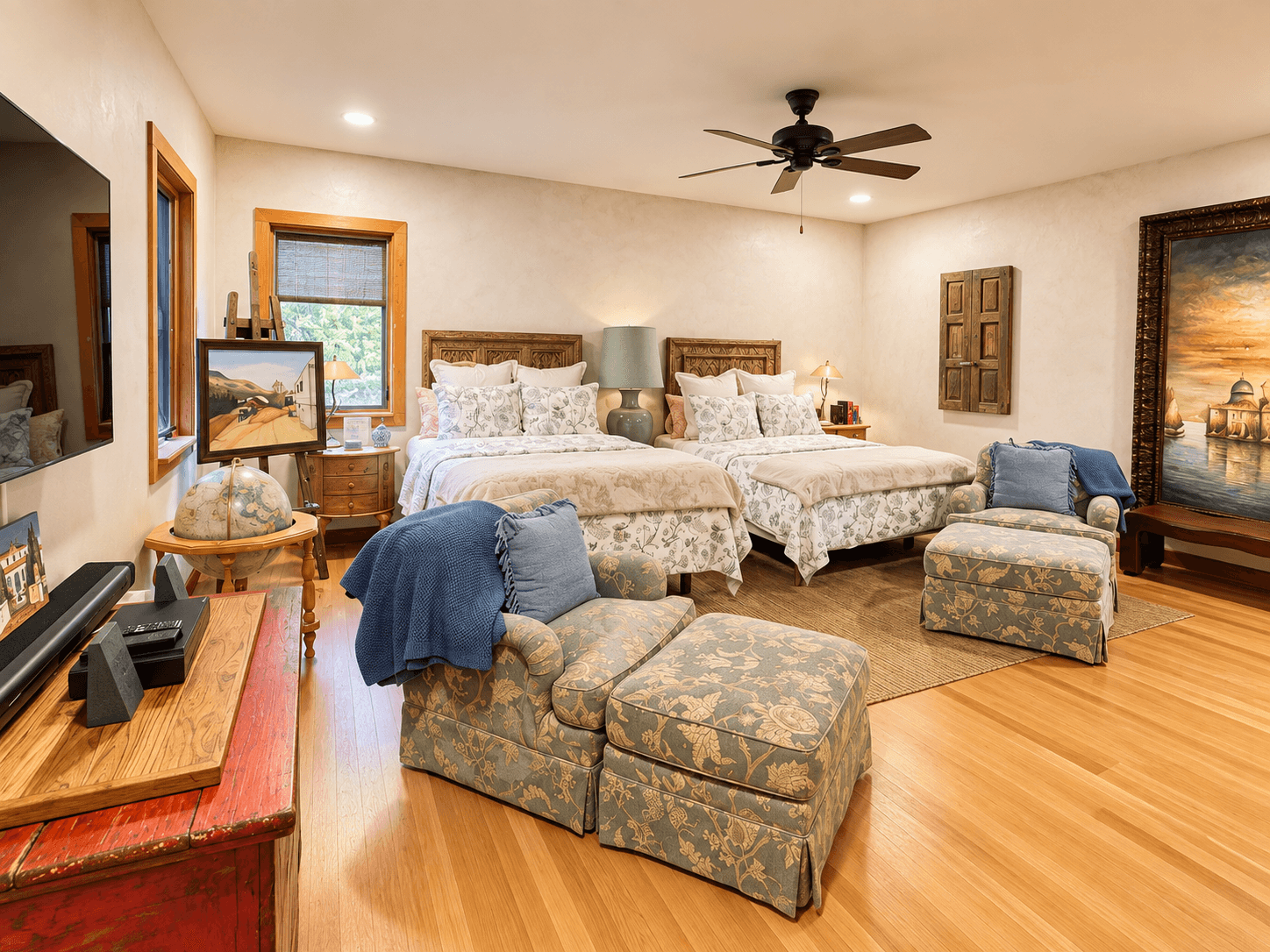 A spacious, elegantly designed bedroom featuring two queen beds, decorative artwork, and comfortable seating.