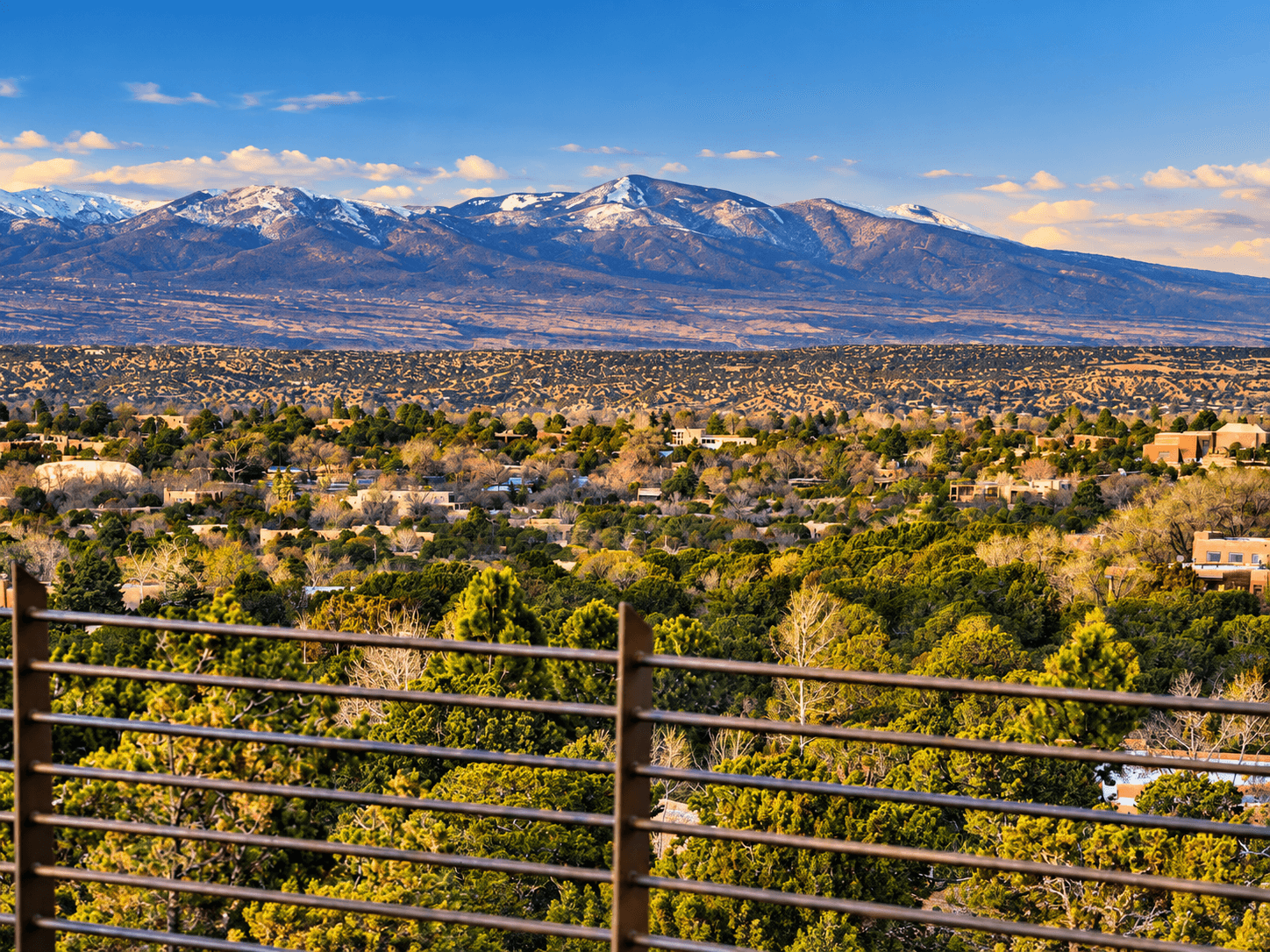 A scenic view of snow-capped mountains overlooking a lush, green landscape under a clear blue sky.