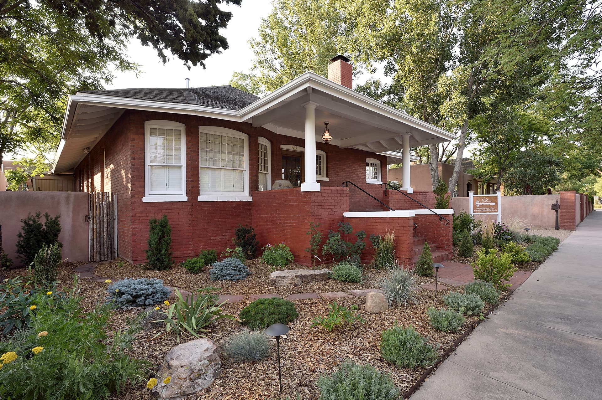 A charming red brick house with a front porch, surrounded by landscaped gardens.
