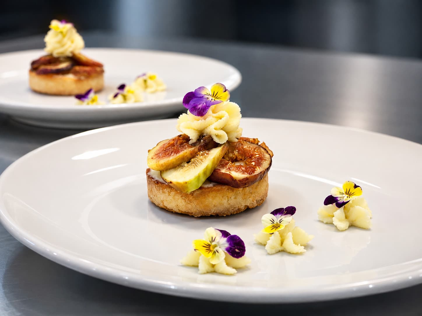 A beautifully plated dessert featuring a pastry topped with fruit, cream, and edible flowers.