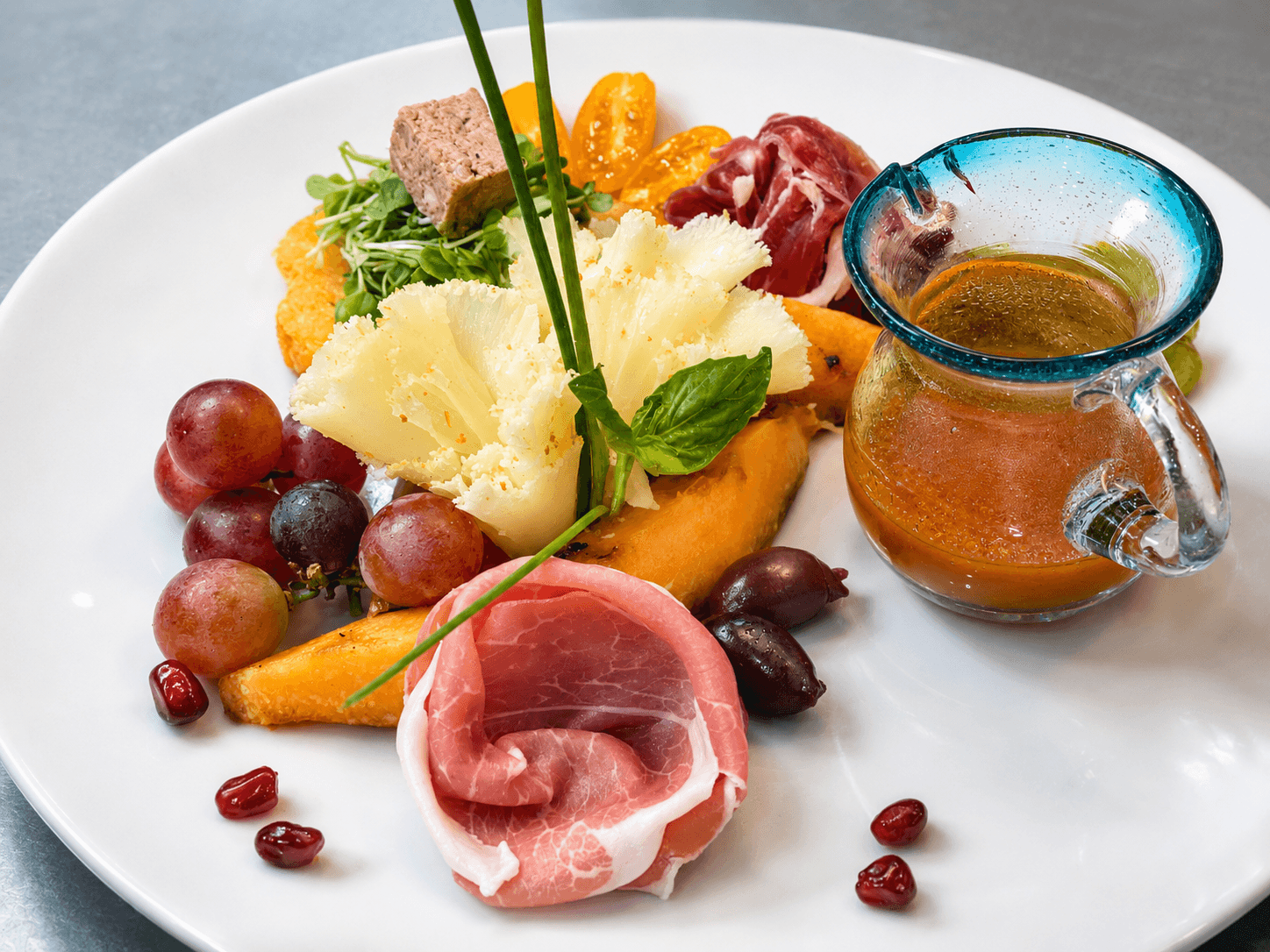 A colorful plate featuring assorted meats, fruits, greens, and a small jug of sauce.