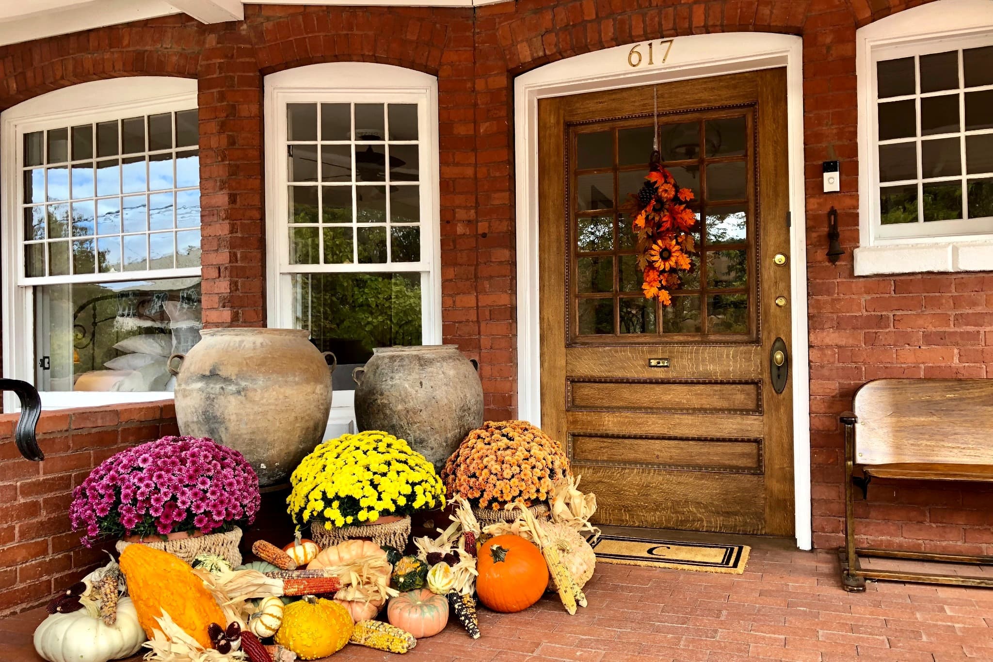 Autumn-themed porch display with colorful mums, pumpkins, and decorative gourds beside a wooden door.