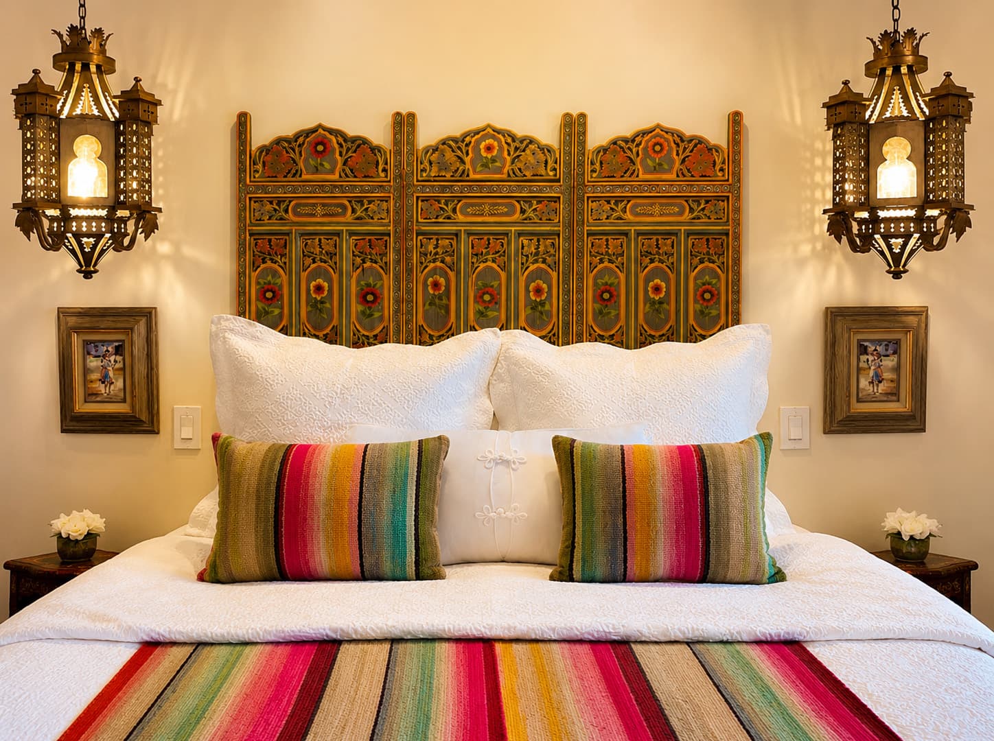 A cozy bedroom featuring a colorful striped blanket, decorative pillows, and ornate wall sconces.