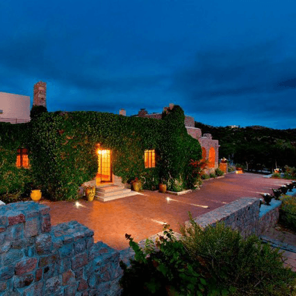 A cozy, ivy-covered stone house illuminated at dusk, surrounded by a lush garden.
