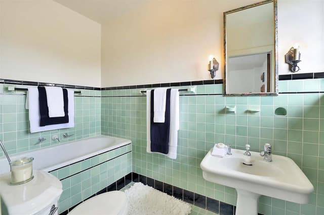A serene bathroom featuring mint green tiles, a bathtub, and elegant fixtures.