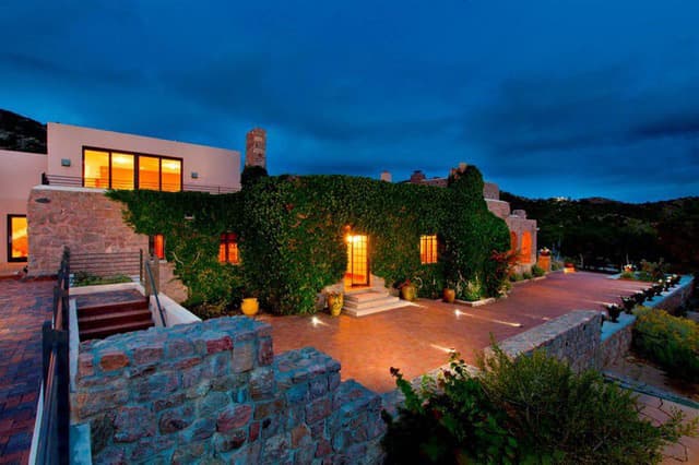 A modern stone house with ivy-covered walls illuminated at dusk.