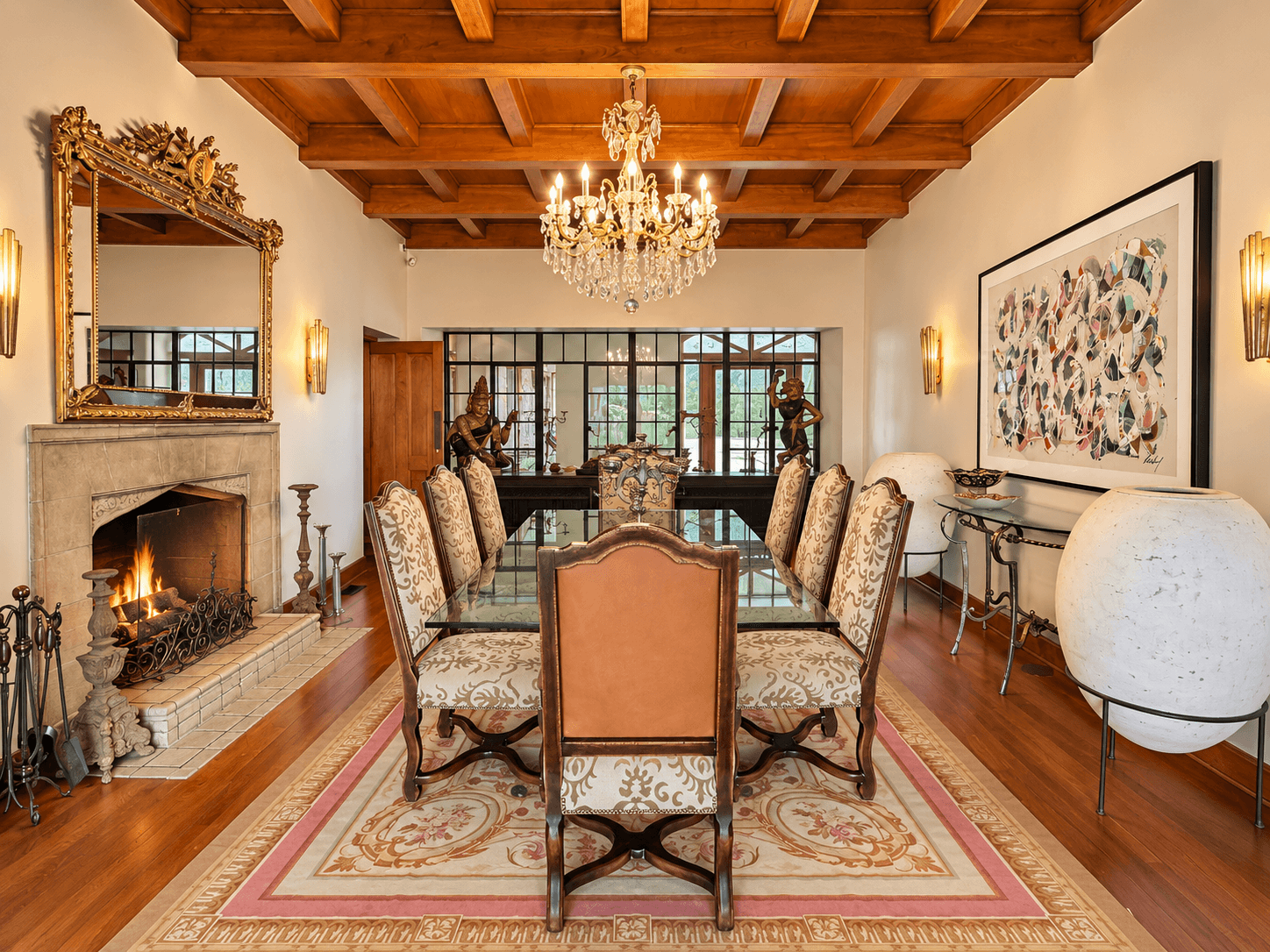 An elegant dining room featuring a glass table, ornate chairs, a chandelier, and a cozy fireplace.