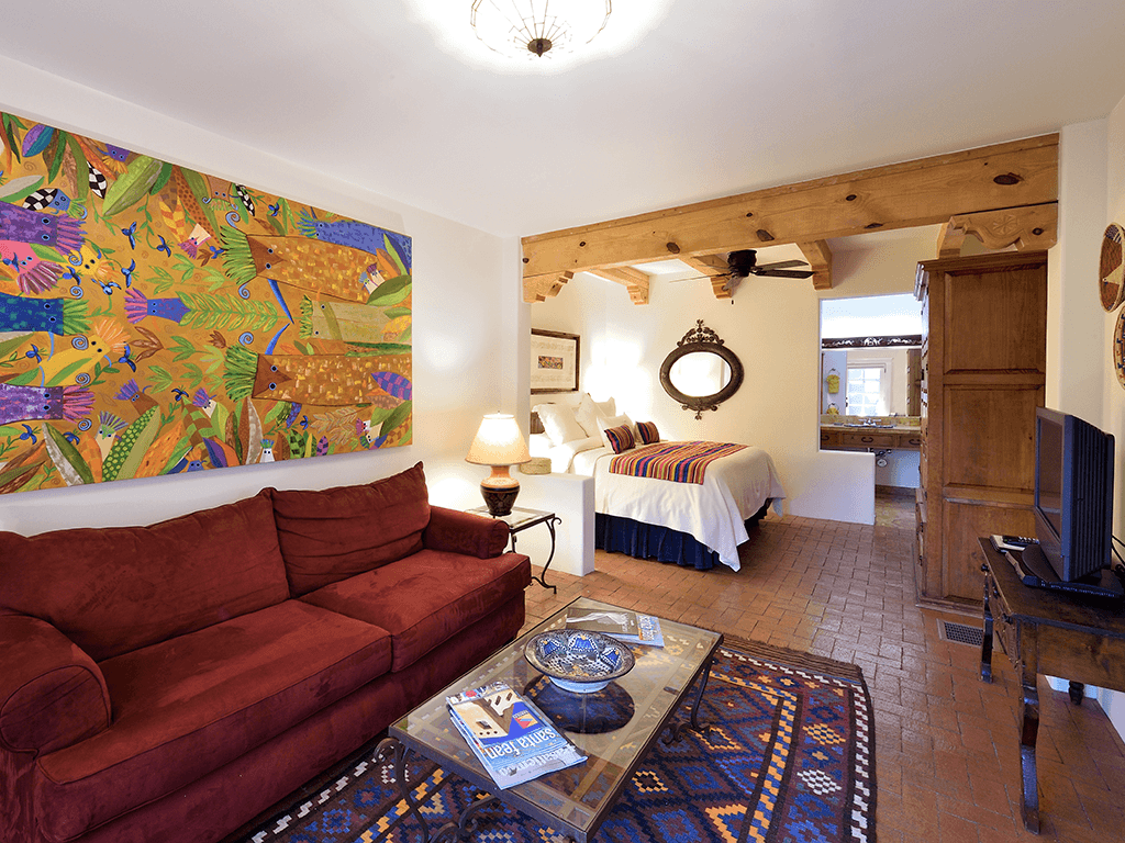 A cozy hotel room featuring a red couch, a colorful wall mural, and a view of a bedroom with white bedding.