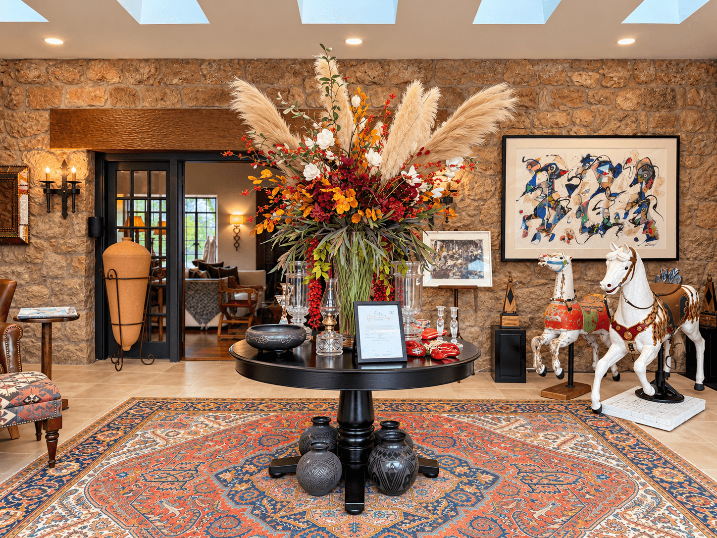 A vibrant floral arrangement sits on a round table in a rustic room adorned with eclectic decor and art.