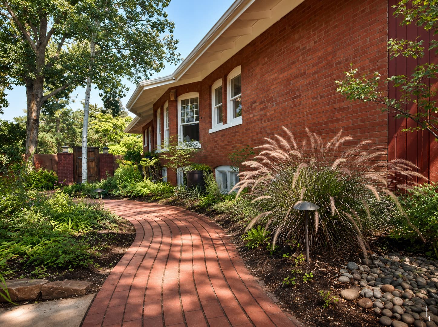 A curving brick pathway bordered by lush greenery leads to a red brick house.
