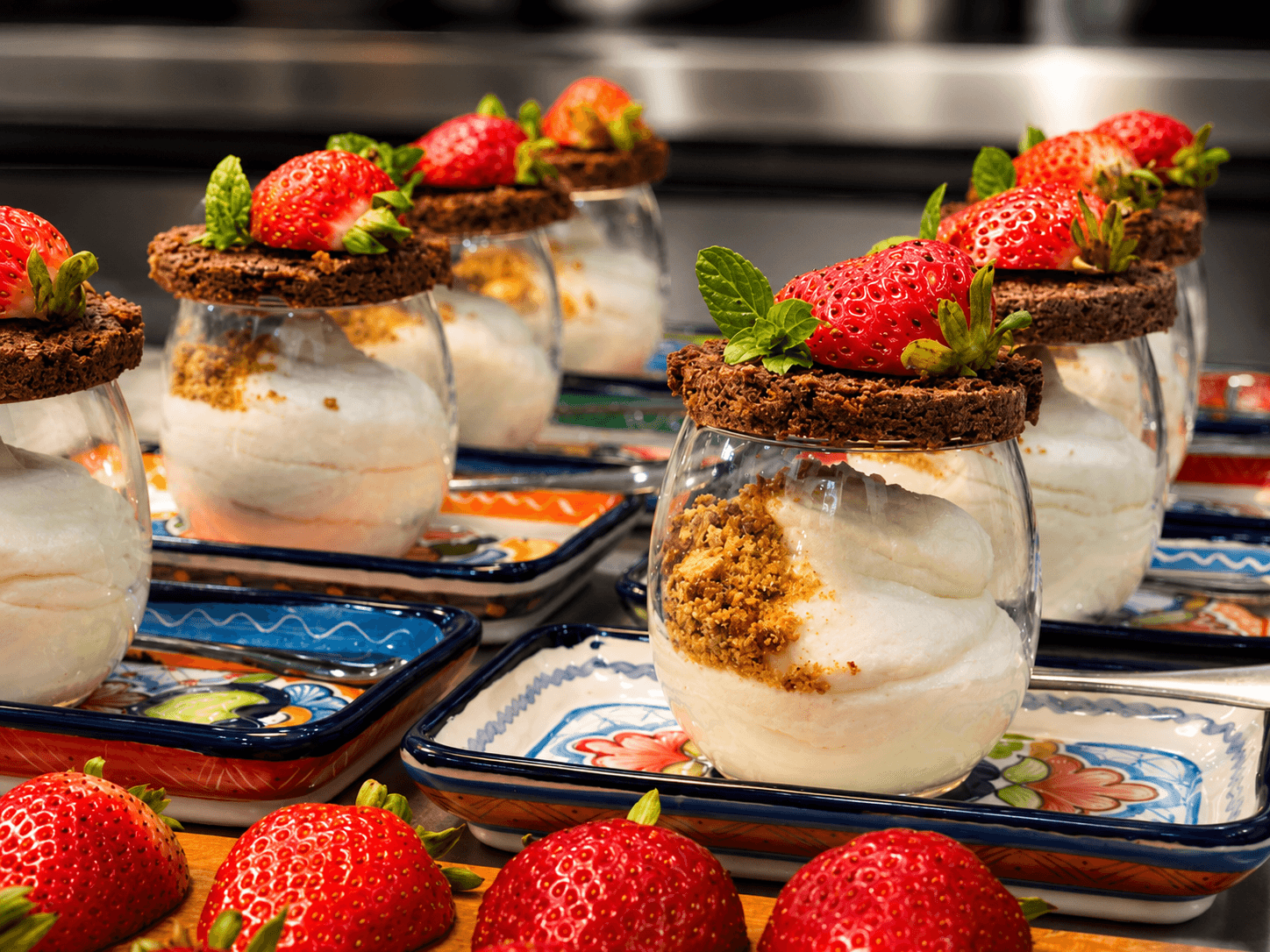 Dessert jars filled with whipped cream, topped with chocolate cookies and strawberries, displayed on colorful plates.