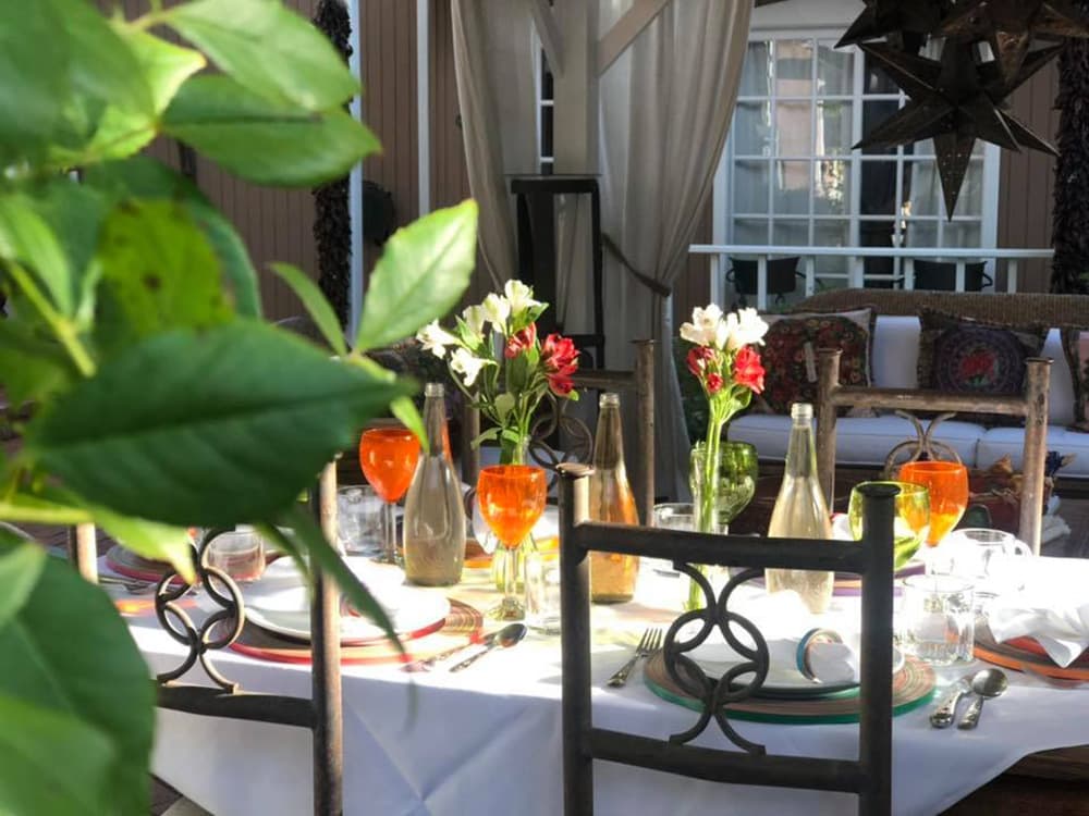 A beautifully set outdoor dining table with colorful glasses and fresh flowers surrounded by greenery.