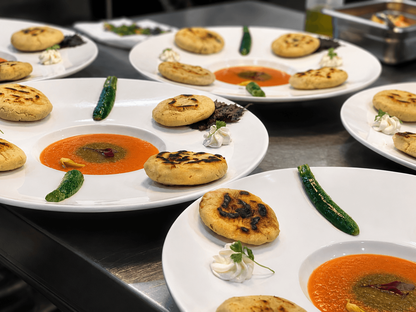Plates of round, grilled flatbreads served with vibrant orange sauce, green chilies, and decorative garnishes.