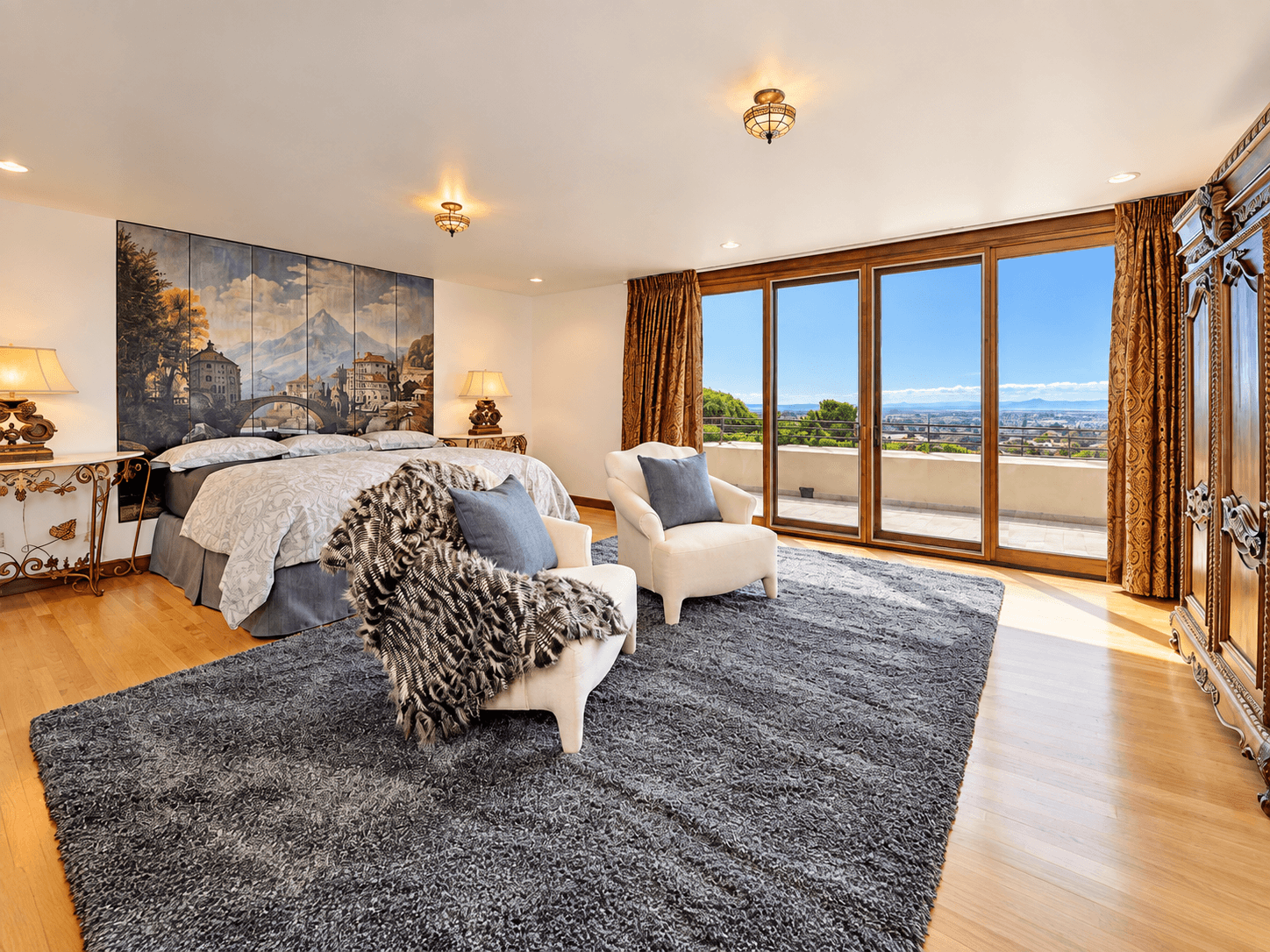 Spacious bedroom featuring a large bed, two armchairs, and extensive windows offering a scenic view.