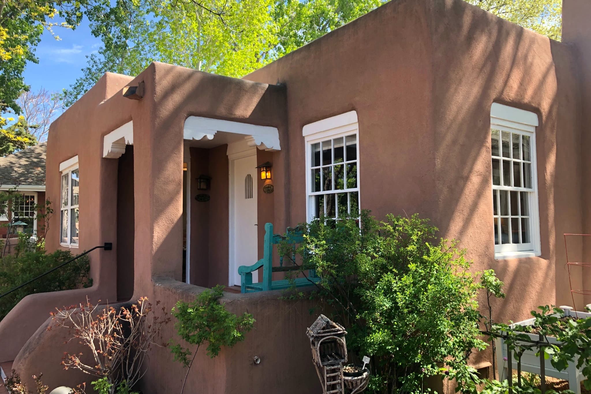 A stucco house with white trim surrounded by green plants.