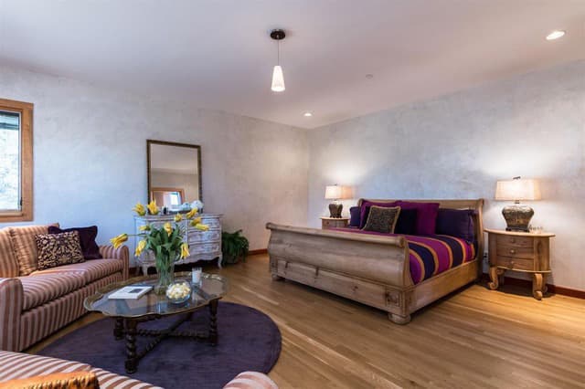 A cozy living space featuring a bed, striped sofa, coffee table with flowers, and warm lighting.