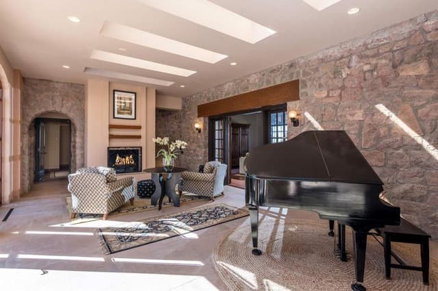 A spacious living room featuring a grand piano, cozy seating, and stone walls.