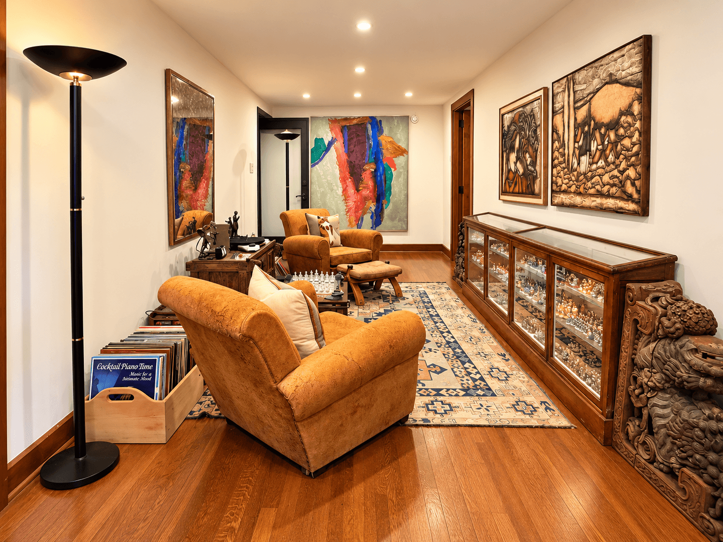 A stylish hallway featuring two comfortable armchairs, a decorated wall, a wooden display case, and warm lighting.