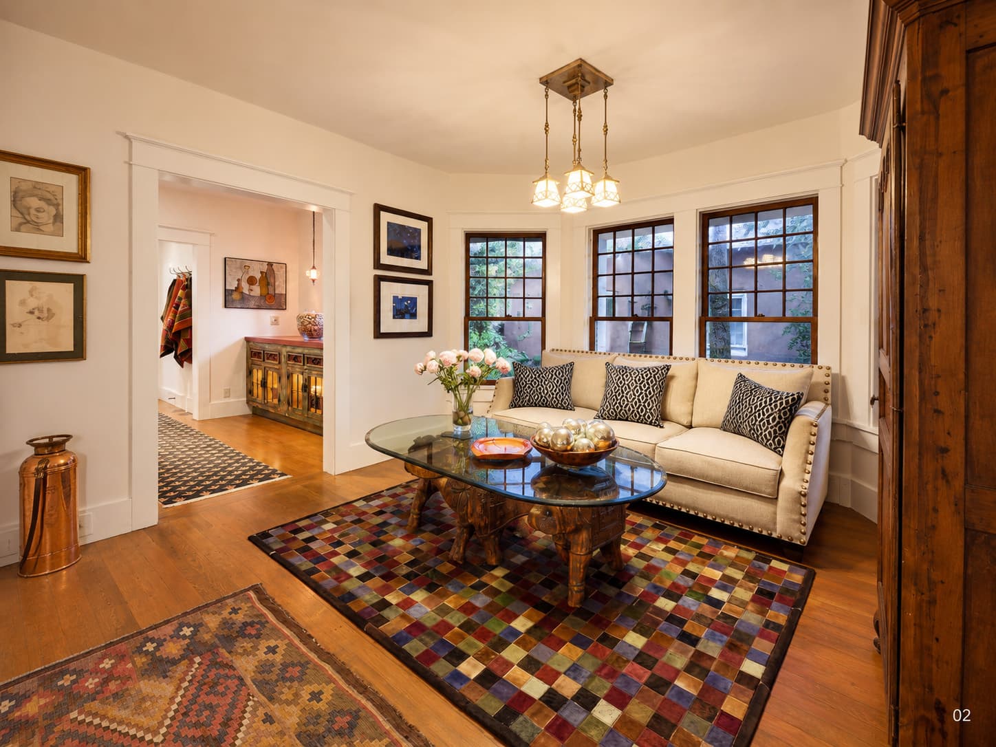 Cozy living room featuring a white couch, colorful rug, and a glass coffee table with flowers.