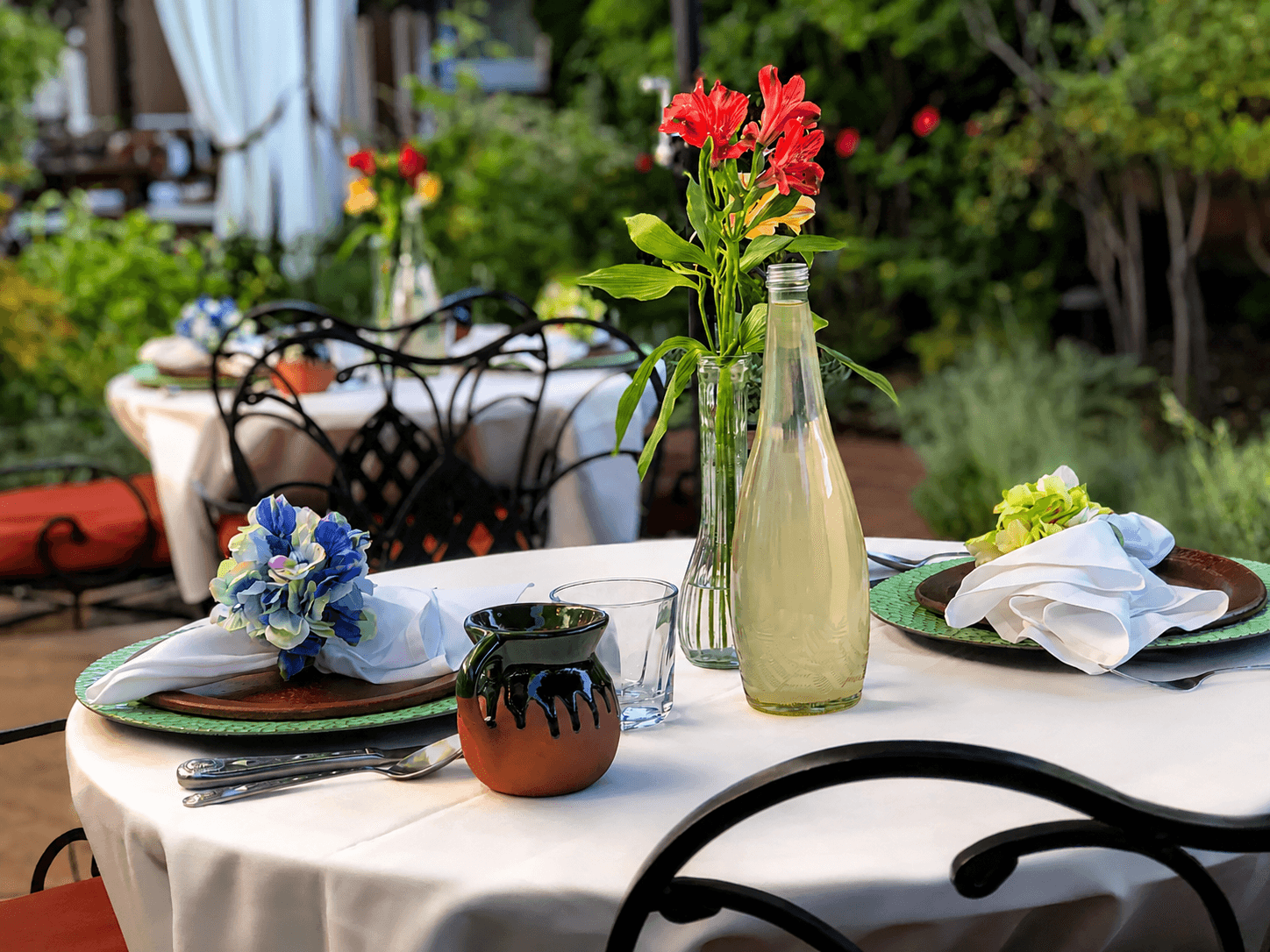 A beautifully set dining table outdoors with floral arrangements, decorative napkins, and glassware.