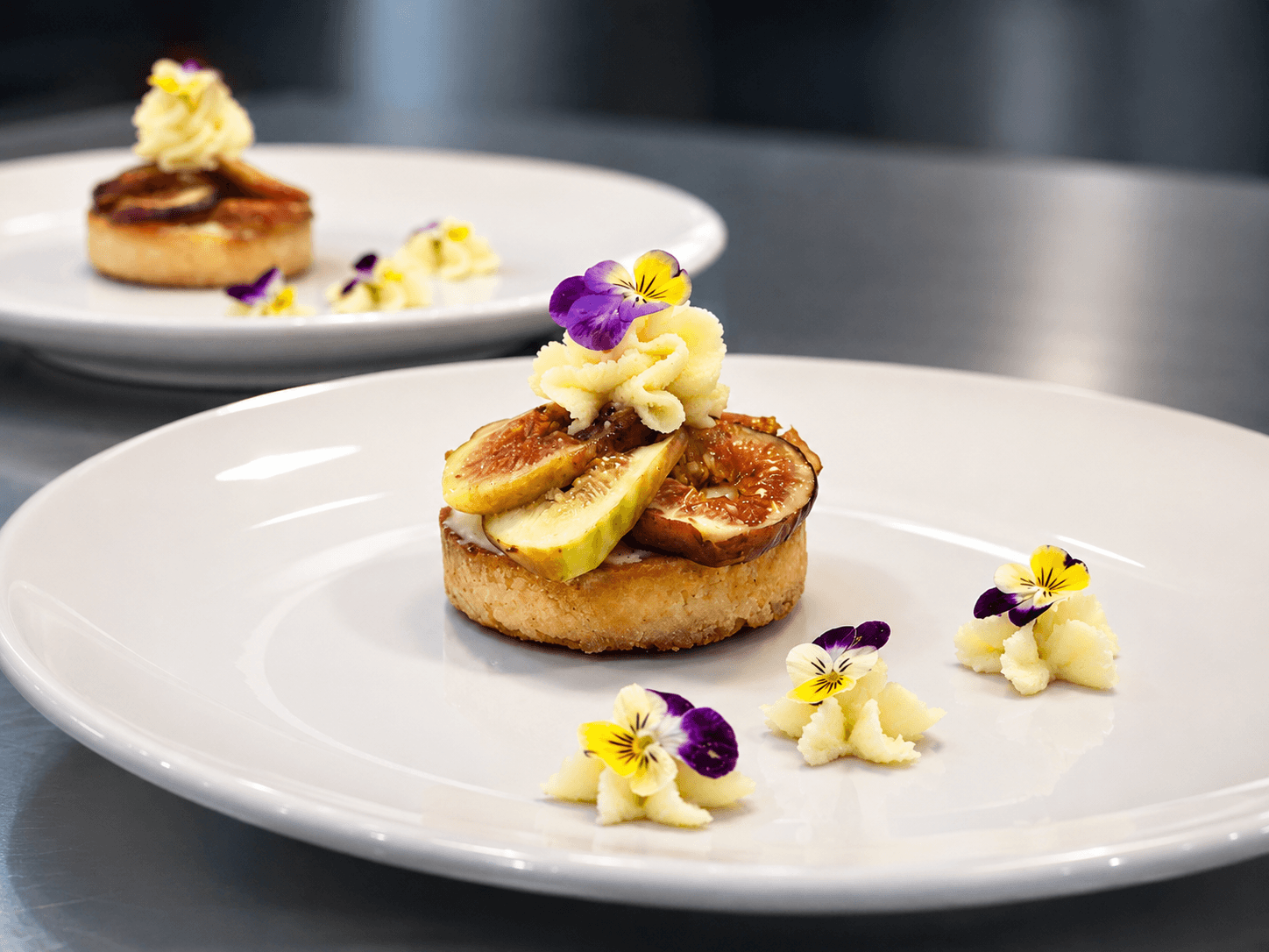 A plated dessert featuring a fig tart topped with cream and edible flowers.