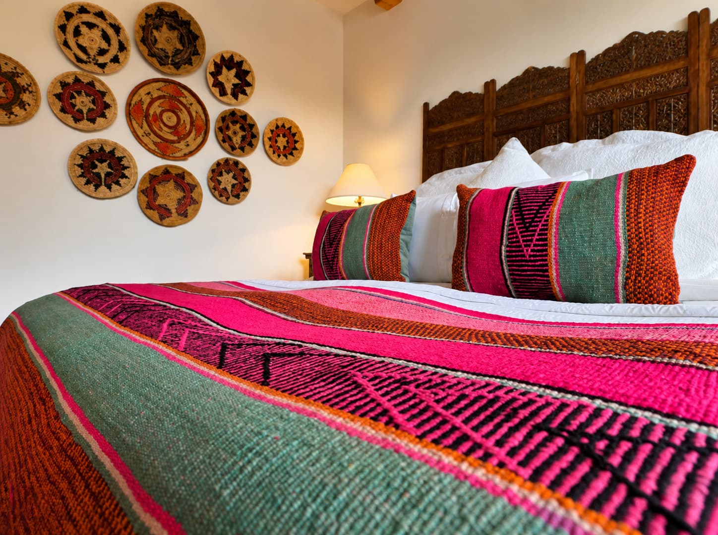 A colorful woven blanket with decorative pillows adorns a bed against a wall of unique round wall art.