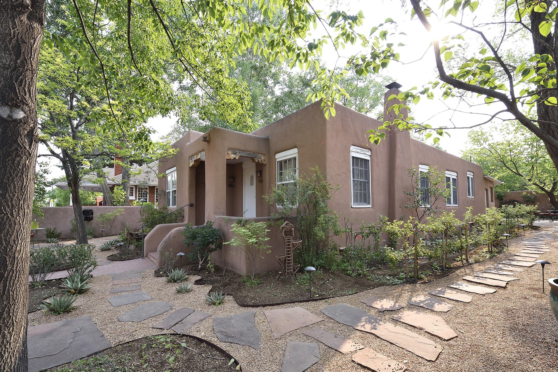 A southwestern-style adobe house surrounded by a landscaped garden and stone pathway.