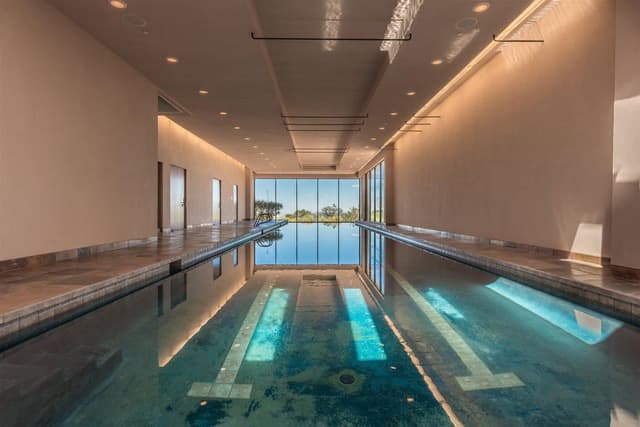 Indoor swimming pool with large windows reflecting natural light.