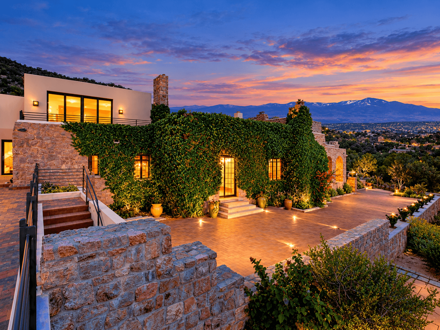 A stone house covered in greenery at sunset, overlooking a mountainous landscape.