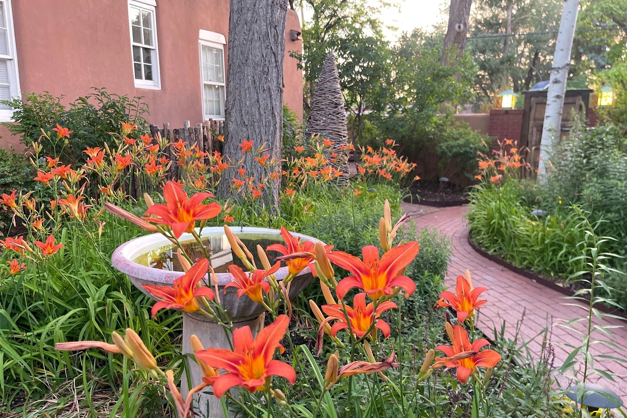 A vibrant garden pathway lined with orange flowers and a water feature.