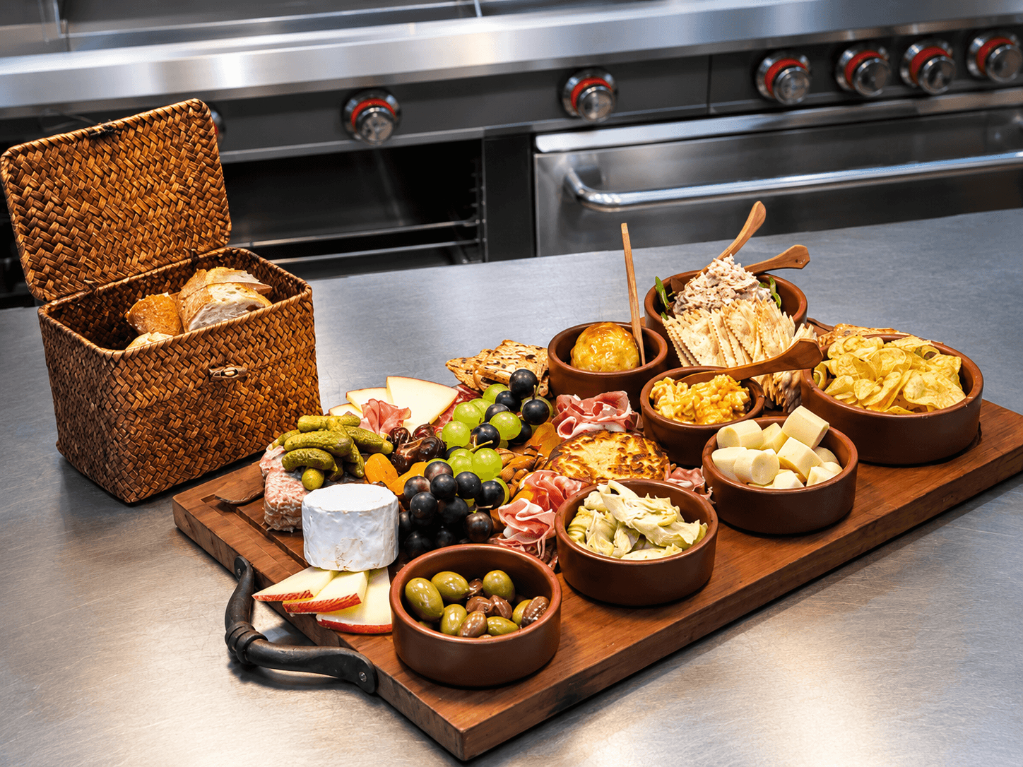 A beautifully arranged charcuterie board featuring meats, cheeses, fruits, pickles, and a basket of bread.