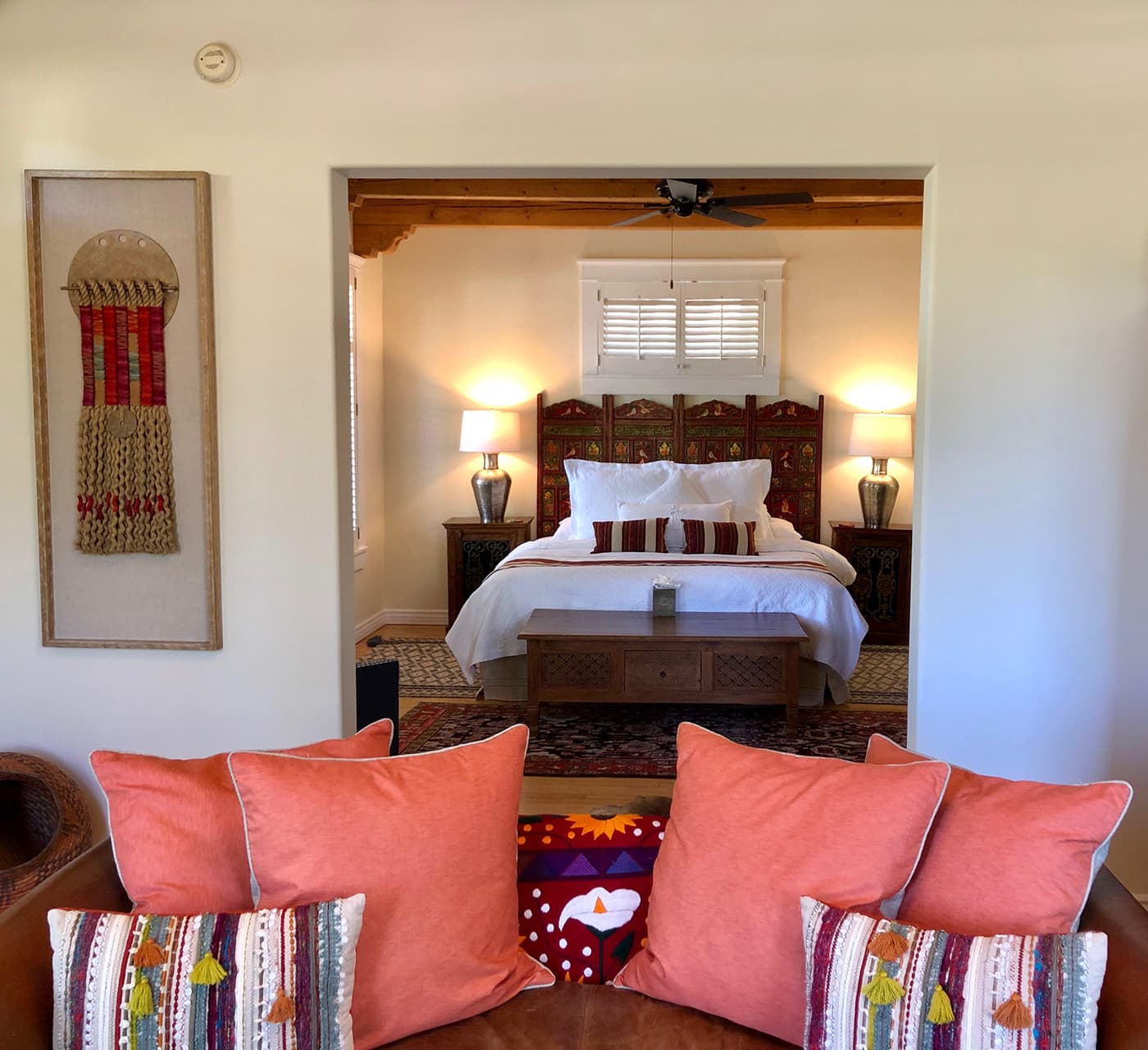 A cozy living space with a view of a warmly lit bedroom featuring decorative pillows and art.